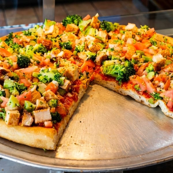 A large pizza with chicken, broccoli, and tomatoes, with one slice removed from the pan.