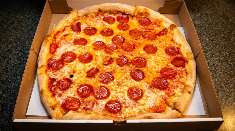 A whole pepperoni pizza with melted cheese and a golden crust sits in a cardboard delivery box.