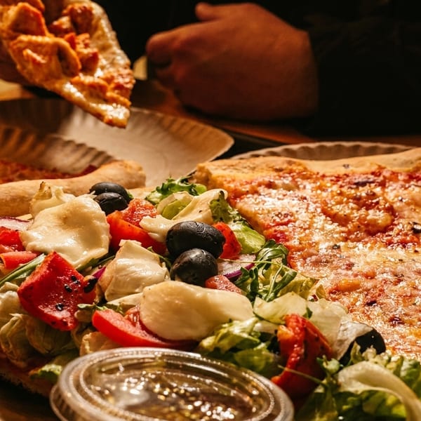 Two large pizza slices, one topped with salad, and a hand holding another slice.