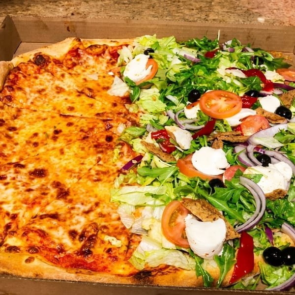 Half cheese pizza and half salad pizza with fresh vegetables in a cardboard box.