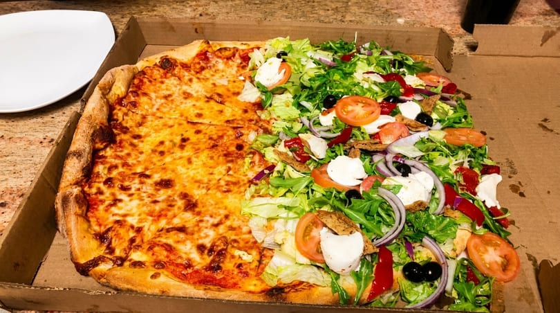 Half cheese pizza and half salad pizza with fresh vegetables in a cardboard box.